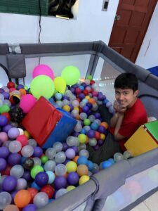 Niño sonriente sentado dentro de una piscina de pelotas plásticas de colores y globos inflables durante una sesión de estimulación e integración sensorial.