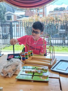 Niño con gafas y camiseta de FunSinapsis realiza actividades de desarrollo cognitivo y motricidad fina utilizando un laberinto de cuentas de madera y fichas de colores sobre una mesa.