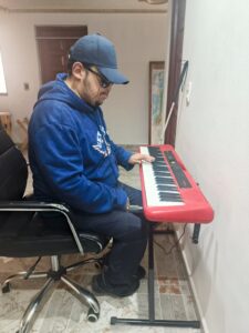 Joven con discapacidad visual toca un teclado electrónico rojo durante un taller de musicoterapia y estimulación sensorial.